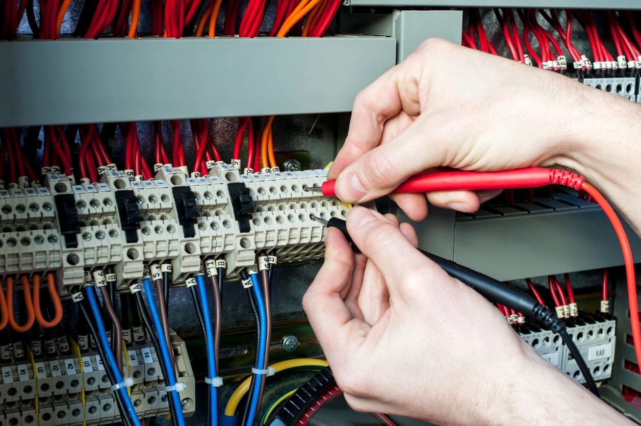 A person is working on wires in an electrical panel.