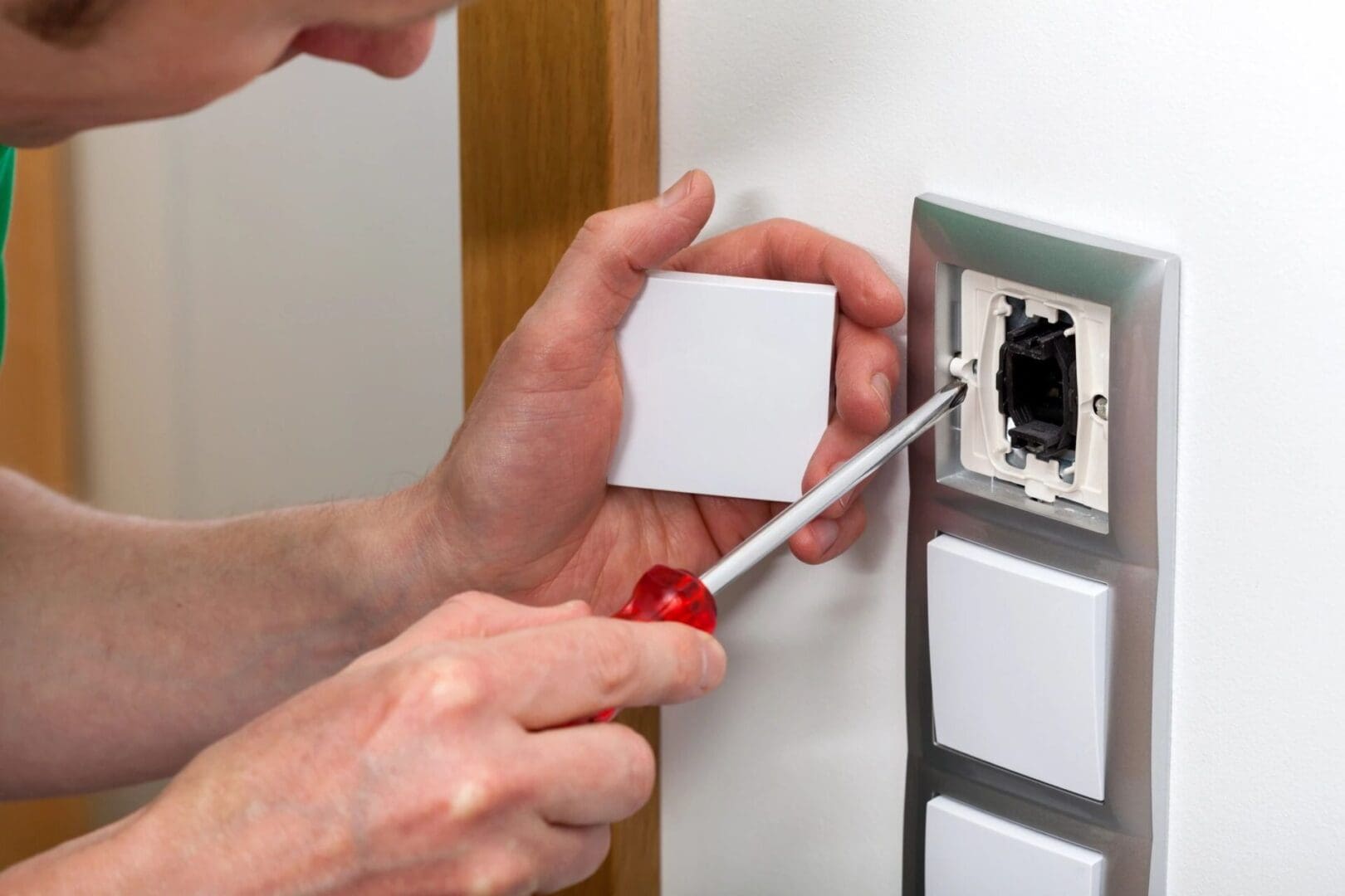 A person is holding a screwdriver and fixing the wall.